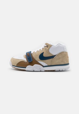 Buty typu mid-top Nike z beżowego zamszu, białej skóry i brązu z niebieskim logo Nike i paskiem na białym tle.