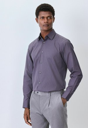Herren Langarmhemd in Lila mit geometrischem Muster, kombiniert mit hellgrauen Hosen. Verfügt über einen Button-Down-Kragen und Knöpfe an der Vorderseite.