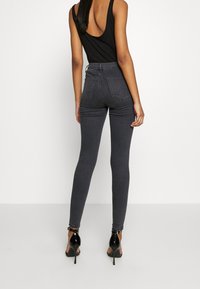 Svart linne, mörkgrå höga smala jeans med bakfickor och slät textur, kombinerat med svarta högklackade skor.