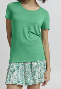 Grön t-shirt med kort ärm och rund halsringning, matchad med en vit kjol med gröna blommönster och lagerdesign.