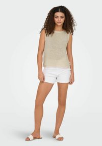 Mouwloze beige gebreide top met een losse pasvorm, gecombineerd met witte shorts. Sandalen hebben een platte zool met een geweven banddesign.