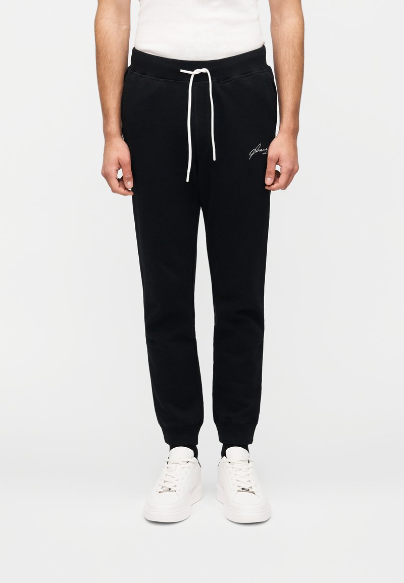 Μαύροι φόρμες με ελαστική μέση και ρυθμιζόμενο κορδόνι. Διαθέτουν λευκό κεντημένο λογότυπο στο αριστερό μπουτόνι. Φοριούνται με λευκά αθλητικά παπούτσια.