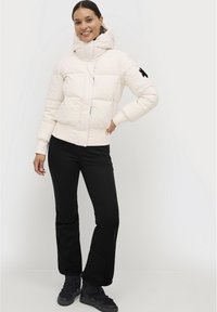 Giacca bianca gonfiata con un colletto alto, zip frontale e due tasche laterali. Abbinata a pantaloni neri e sneaker nere.