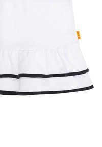 Witte kleding met een uitlopende zoom, voorzien van zwarte accenttrim aan de randen. Inclusief een klein geel label met de tekst "Steiff." Gladde textuur.