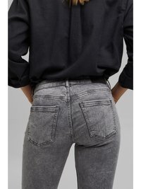 Jeans de denim cinza com uma textura desbotada, design de cinco bolsos e detalhes de costura visíveis. Usados com uma camisa preta, mostrando uma vista traseira.