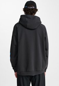 Hoodie i mörkgrått, med en känguru ficka, ribbade ärmslut och nederkant, med en blå accent på vänster ärm. Slät textur.