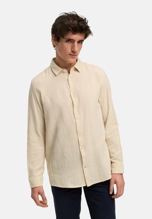 Camisa beige de manga larga hecha de una tela texturizada, con cierre de botones en el frente, cuello clásico y un corte relajado.