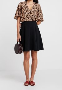 Blouse met luipaardprint en korte mouwen met een V-hals, gecombineerd met een zwarte A-lijn rok. Accessoires zijn een ronde bordeauxrode handtas en rode sandalen.