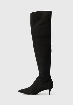 Botte noire en daim au-dessus du genou avec un bout pointu et un petit talon kitten sur un fond gris clair uni.