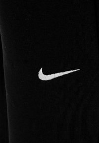 Zwarte stoffen joggers met een witte geborduurde Nike Swoosh-logo aan de linkerkant. Glad textuur met een aansluitend ontwerp.