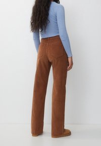 Bruna kordflors vidbena byxor med hög midja, med två bakfickor. Kombineras med en ljusblå ribbad långärmad topp.