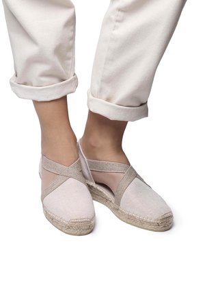 Beige canvas espadrilles with elastic cross straps and jute soles, featuring a closed toe and open sides for breathability.