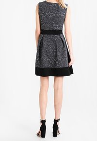 Schwarzes und weißes gemustertes ärmelloses Kleid mit einer figurbetonten Taille und schwingendem Rock, mit einem einfarbigen schwarzen Saum und strukturiertem Stoff.