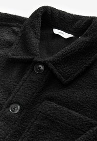 Schwarze, strukturierte Jacke mit Kragen, vorderem Knopfverschluss und einer Brusttasche. Hergestellt aus weichem, fusseligem Material mit sichtbaren Nähten.