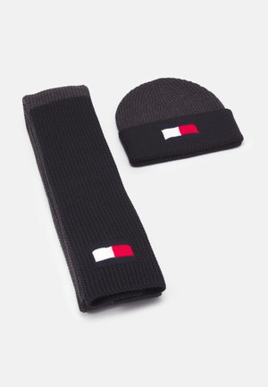 Ensemble écharpe tricotée gris foncé et bonnet avec bordure noire, chacun arborant un patch logo rectangulaire blanc, rouge et bleu marine.
