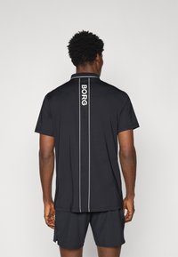 Svart polo skjorte laget av glatt materiale, med en hvit vertikal stripe og "BORG" trykt langs ryggen. Korte ermer, klassisk krage.