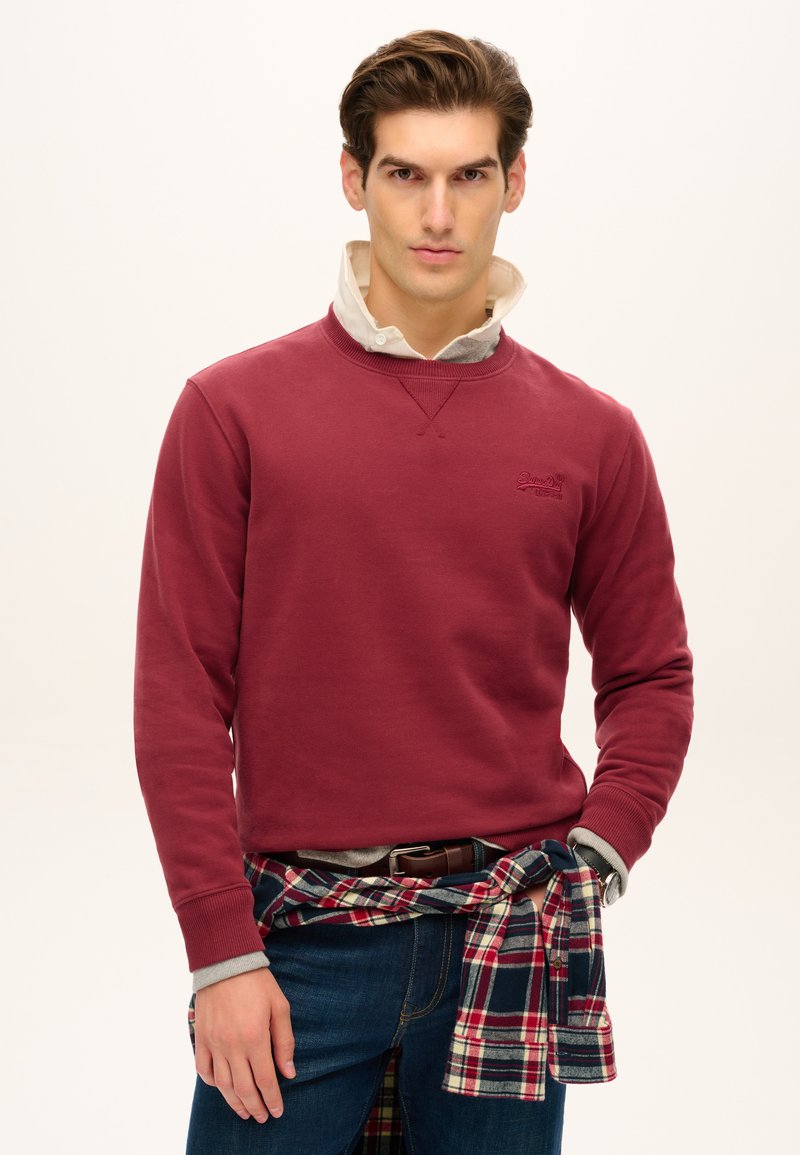 Marlot sweatshirt med rund hals og ribbede manchetter, lagd over en grå skjorte med krave. Parret med mørkeblå jeans og en ternet skjorte bundet omkring taljen.