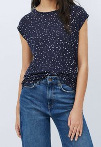 Navy blue short-sleeve top with white dot pattern, soft fabric, crew neckline, paired with light blue jeans. Casual and fitted style.