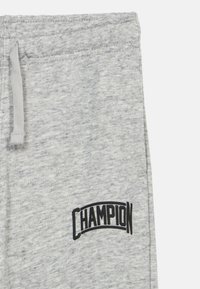 Γκρι φόρμες κατασκευασμένες από βαμβακερό μείγμα με ελαστική μέση και κορδόνι. Διαθέτουν μαύρο λογότυπο "CHAMPION" στο μηρό.