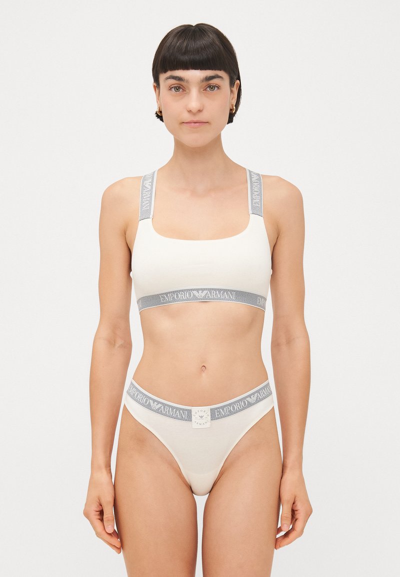 Cream-colored bra and thong set made of soft fabric with gray branded elastic straps. Features a square neckline and minimalistic design.