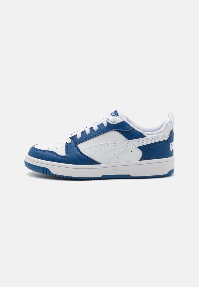 Witte en blauwe sneaker met een bovenkant van soepel leer, geperforeerde neus, vlakke witte veters en een gewatteerde kraag. Beschikt over een rubberen zool.