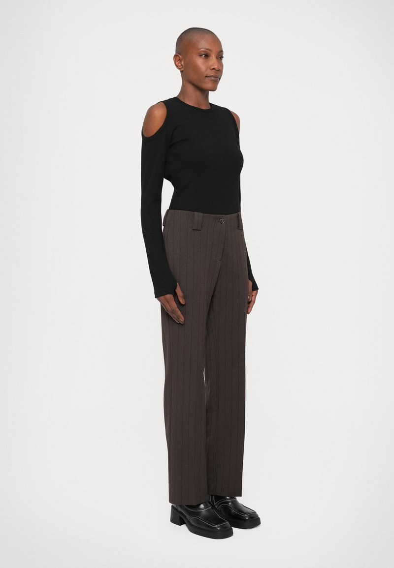 Haut noir à épaules dénudées à manches longues associé à un pantalon à rayures brunes et des chaussures noires imposantes. Texture de tissu lisse et coupe ajustée.