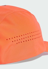 Casquette orange en tissu léger et texturé. Elle comprend un panneau avec des trous de ventilation régulièrement espacés et une visière courbée.