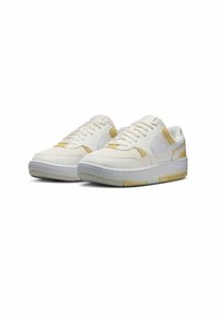 Zapatillas blancas con detalles dorados, presentan una parte superior de tela texturizada, lengüeta acolchada y suela de goma con un patrón de banda de rodadura distintivo.