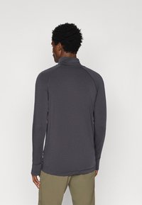 Szürke, hosszú ujjú póló, magas gallérral, raglán ujjakkal és sima textúrával. Az alsó szegély enyhén ívelt.