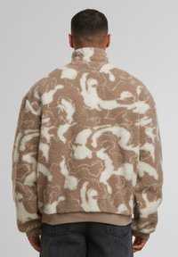 Giacca soffice beige e crema con motivo, colletto alto e orlo a coste; realizzata in un morbido tessuto testurizzato con una vestibilità ampia.