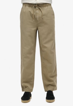 Pantaloni khaki larghi in cotone morbido. Presentano una vita elastica con cordoncino e orli cuffati. Davanti piatto, senza tasche visibili.