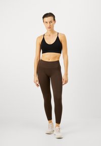 Barna leggings fekete sportmelltartóval párosítva. A leggings magas derékkal és sima textúrával rendelkezik. Világos színű sportcipők egészítik ki az öltözéket.
