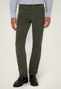 Oliwkowe spodnie w prążek o dopasowanym kroju, z przednimi kieszeniami i zapięciem na guzik, połączone z ciemnobrązowymi mokasynami.