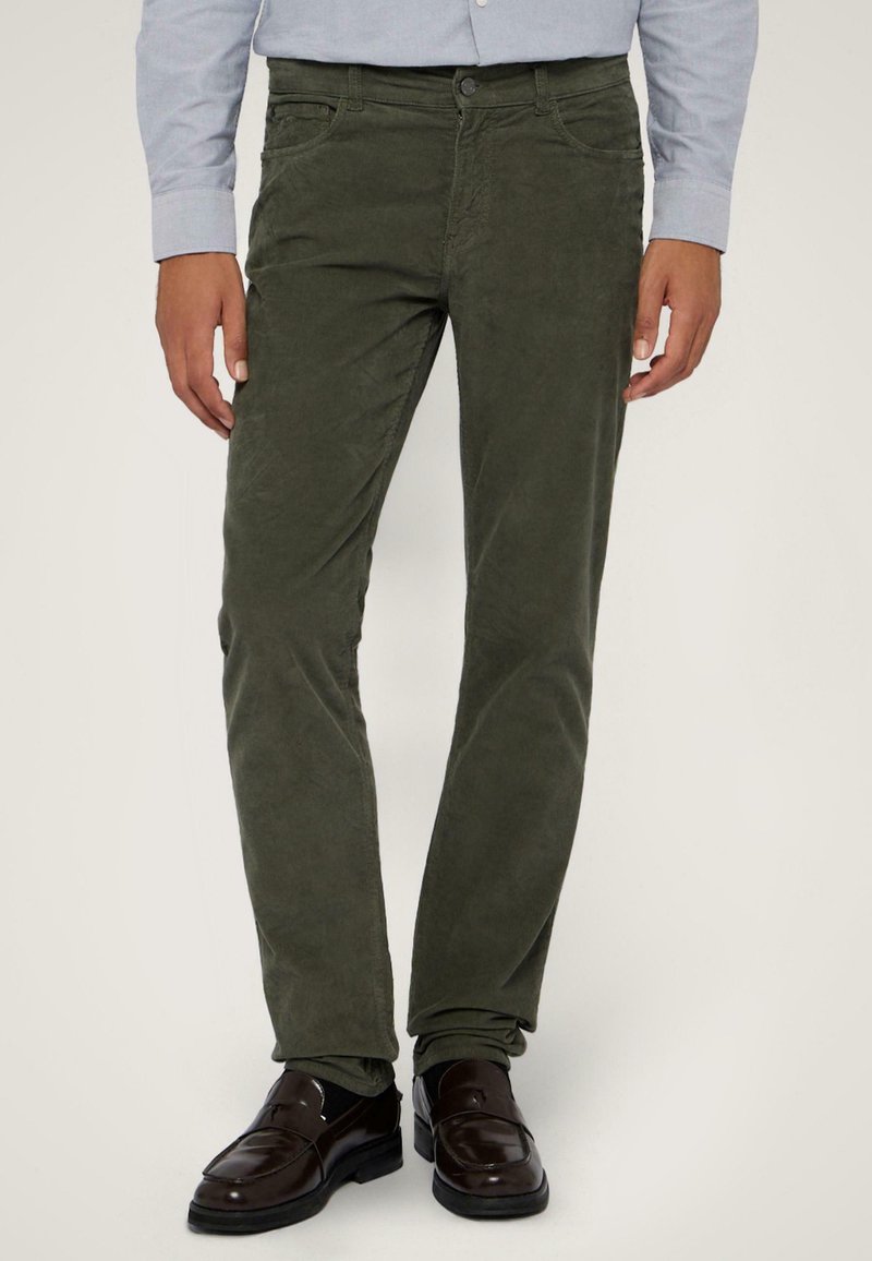 Oliwkowe spodnie w prążek o dopasowanym kroju, z przednimi kieszeniami i zapięciem na guzik, połączone z ciemnobrązowymi mokasynami.