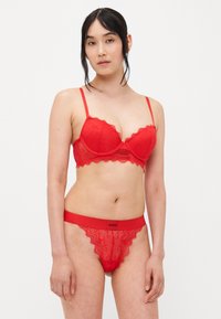 Ensemble de lingerie en dentelle rouge comprenant un soutien-gorge à bordure festonnée avec armatures et bretelles réglables, associé à une culotte assortie ornée de dentelle.