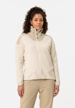 Beige fleece jacket with a high collar, front zipper, two pockets, and contrasting shoulder panels. Features soft texture and relaxed fit.