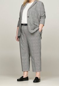 Šedý kostkovaný blejzr a odpovídající zkrácené kalhoty vyrobené z texturované látky, doplněné bílým topem a černými mokasíny.