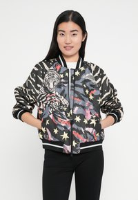 Cazadora bomber con base negra, que presenta una mezcla de estampados de animales, estrellas y patrones vibrantes. Puños y dobladillo acanalados, cierre de cremallera.