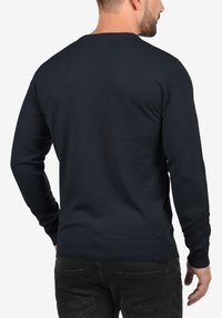 Marineblauer gestrickter Pullover mit langen Ärmeln sowie gerippten Bündchen an Ärmelenden und Saum. Verfügt über einen klassischen Rundhalsausschnitt und eine glatte Textur.