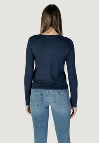Pull-over en laine bleu marine à manches longues avec un col rond, design ajusté et ourlet côtelé, associé à un jean en denim bleu clair avec des poches arrière.