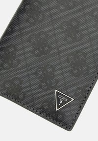 Billetera negra con diseño, fabricada en material texturizado, que presenta un sutil patrón de logo y un acento metálico triangular con el nombre de la marca.