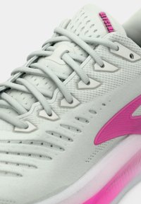 Šviesiai pilkas sportinis batelis su rožiniais akcentais, turintis akių tinklo viršutinę dalį, suvarstymą raišteliais, tekstūruotus elementus ir storą baltą bei rožinę pado dalį.