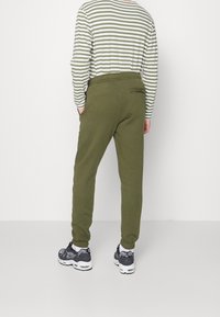 Joggers i olivgrönt med avslappnad passform, utrustade med en bakficka och elastiska muddar, kombinerade med en randig långärmad skjorta.