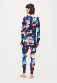 Vešbarvna telovadna garnitura z dolgimi rokavi in legginsom v vzorcu, ki spominja na oblake, izdelana iz gladkega, raztegljivega blaga.