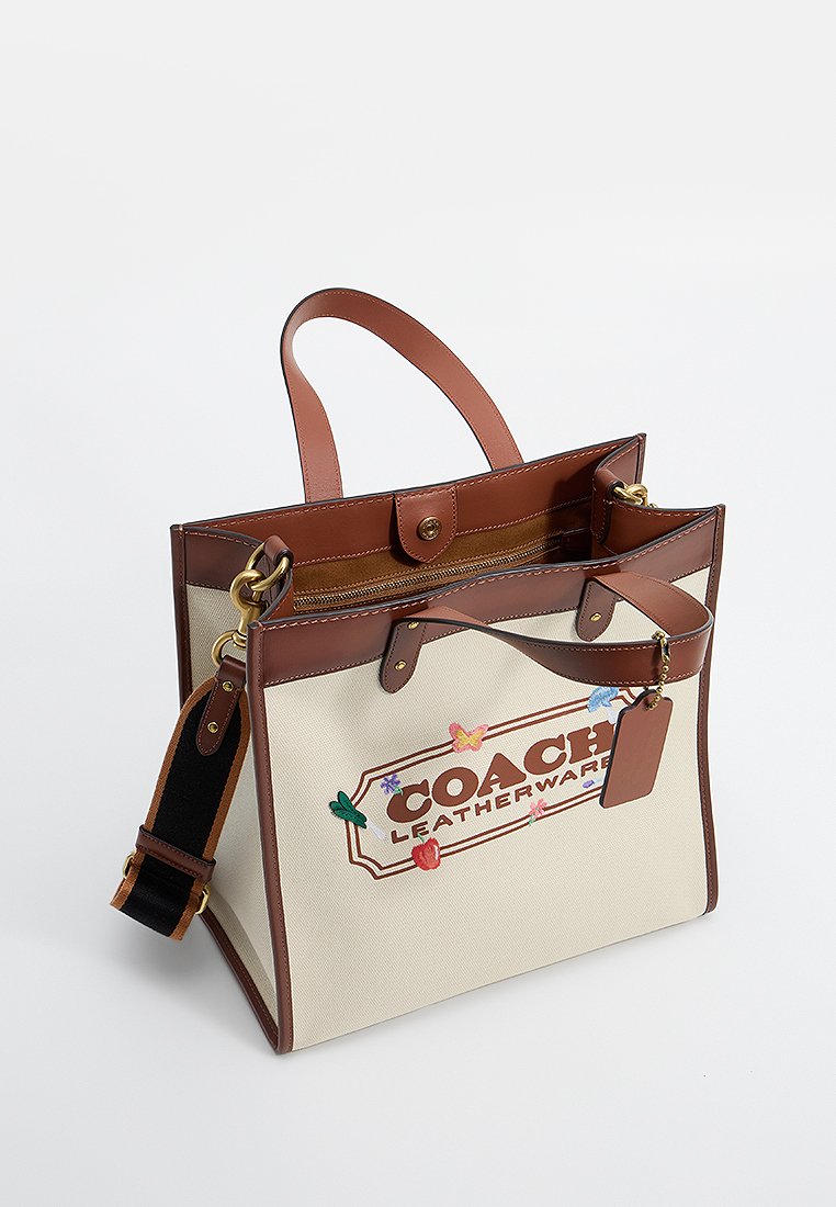 Bolso de lona con acentos de cuero marrón, patrones florales bordados, asas superiores y una correa de hombro desmontable. Cuenta con un cierre a presión.