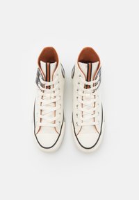 Wysokie trampki z płótna w kolorze off-white, z pomarańczowym wnętrzem, czarnymi akcentami i metalowymi oczkami oraz białymi sznurowadłami.