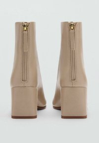 Beige ankelstøvler med blokhæl, glat tekstur, sidelukninger og et minimalistisk design.