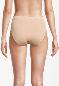 Vista posteriore di una persona che indossa mutande beige a vita alta, in piedi con le braccia rilassate ai lati su uno sfondo bianco.