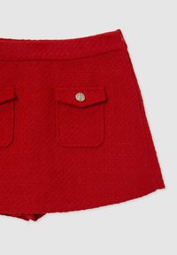 Mini gonna in tessuto intrecciato rosso con due tasche frontali, ciascuna con una fibbia dorata decorativa. Forma A-line semplice e finitura testurizzata.