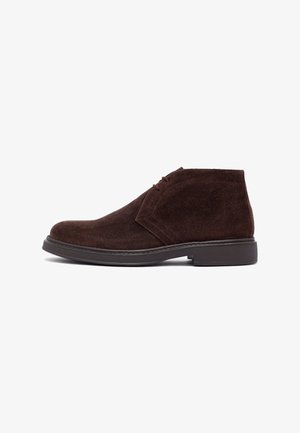 Bottines désert en daim brun foncé pour homme avec fermeture à lacets et semelle en caoutchouc noire, présentées de profil sur un fond blanc.